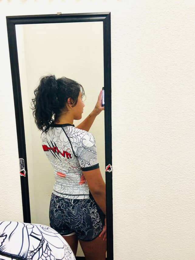 Woman wearing Rising Dragon female grappling shorts and rash guard taking mirror selfie
