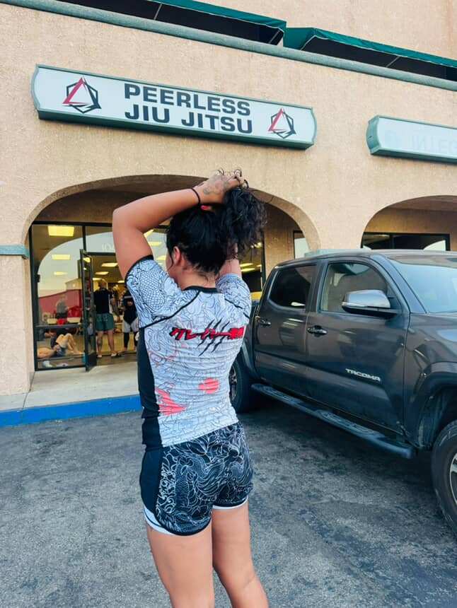 Woman wearing Rising Dragon BJJ Nogi Set rash guard and shorts standing outside Peerless Jiu Jitsu gym