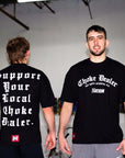 Two men wearing black t-shirts with text, one facing forward and one back, in an indoor setting.