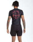 Person wearing a black Bjj rash guard set with red death cuddles Jiu Jitsu graphics on the back, standing against a white background.
