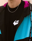 Close-up of the collar and chest area, showing the magenta mesh hood lining and a silver chain over a black BJJ logo t-shirt, framed by the black and teal windbreaker jacket.