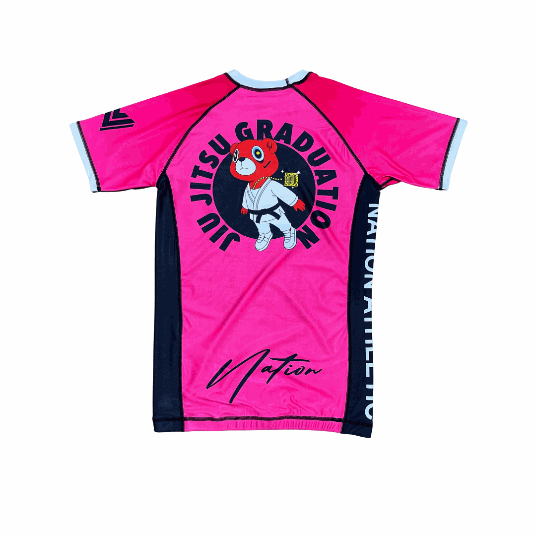 Kanye BJJ Rash Guard in pink with black panels, featuring a cartoon bear in a gi and "Jiu Jitsu Graduation" text on the back, made from moisture-wicking fabric for no-gi training