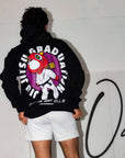 Person wearing a black hoodie with a colorful graphic design on the back, standing against a white wall.