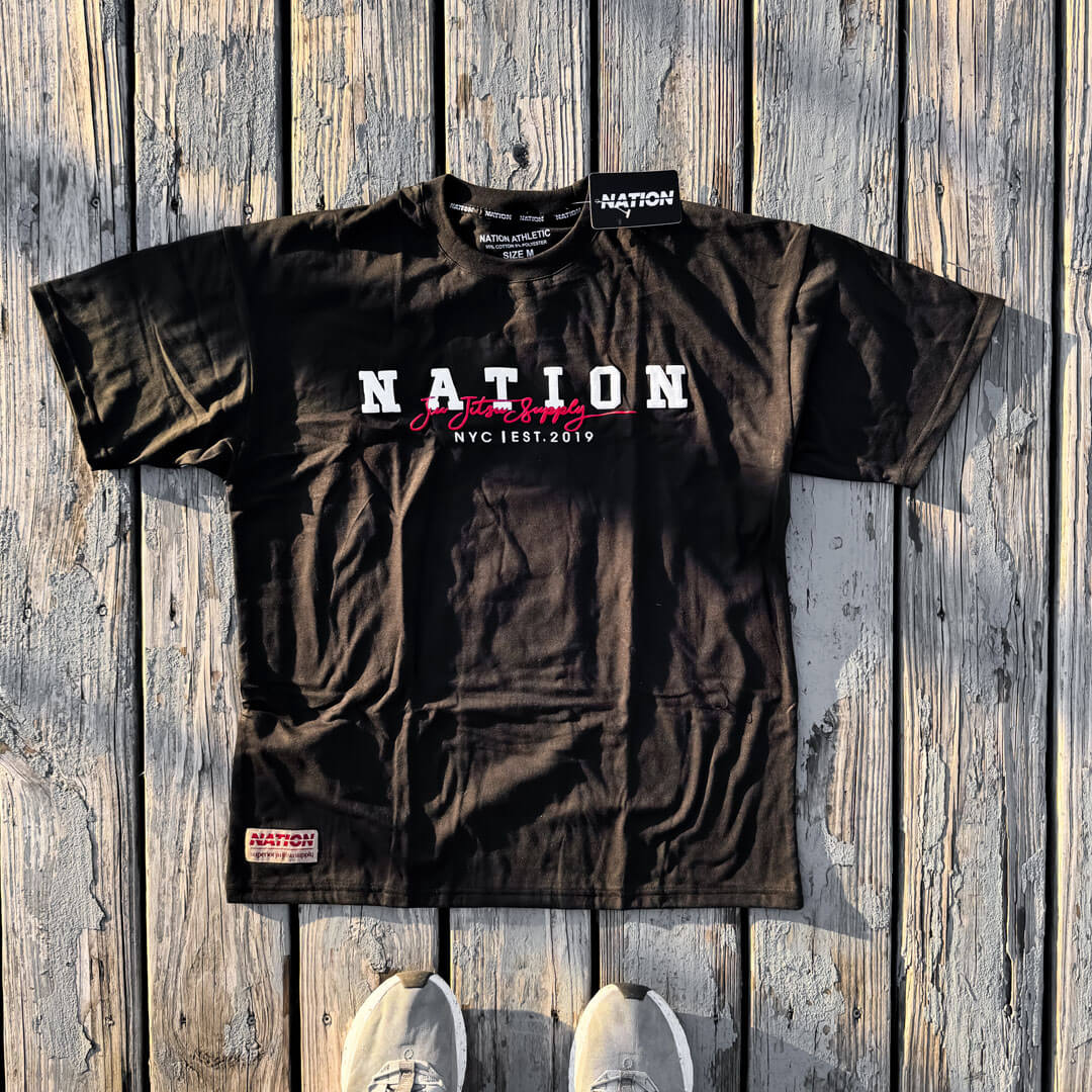 Black Nation Varsity BJJ T-shirt with oversized fit and 3D puff print design on wooden background.