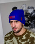 Man wearing a blue beanie with 'NATION' text, standing against a blurred background.