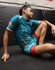 Person in a blue athletic outfit with red accents sitting on a black mat.