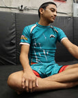Person sitting on a mat in a martial arts or fitness studio wearing a blue athletic outfit.