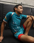 Person wearing a blue sports outfit with red accents, sitting on a black mat.