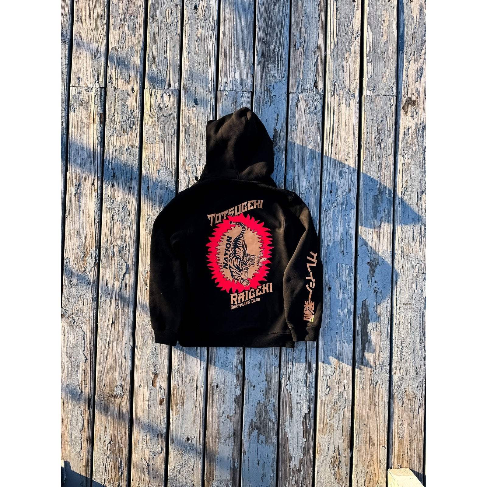 Black Totsugeki BJJ Hoodie with screen-printed design, ultra-soft fleece, on wooden background.
