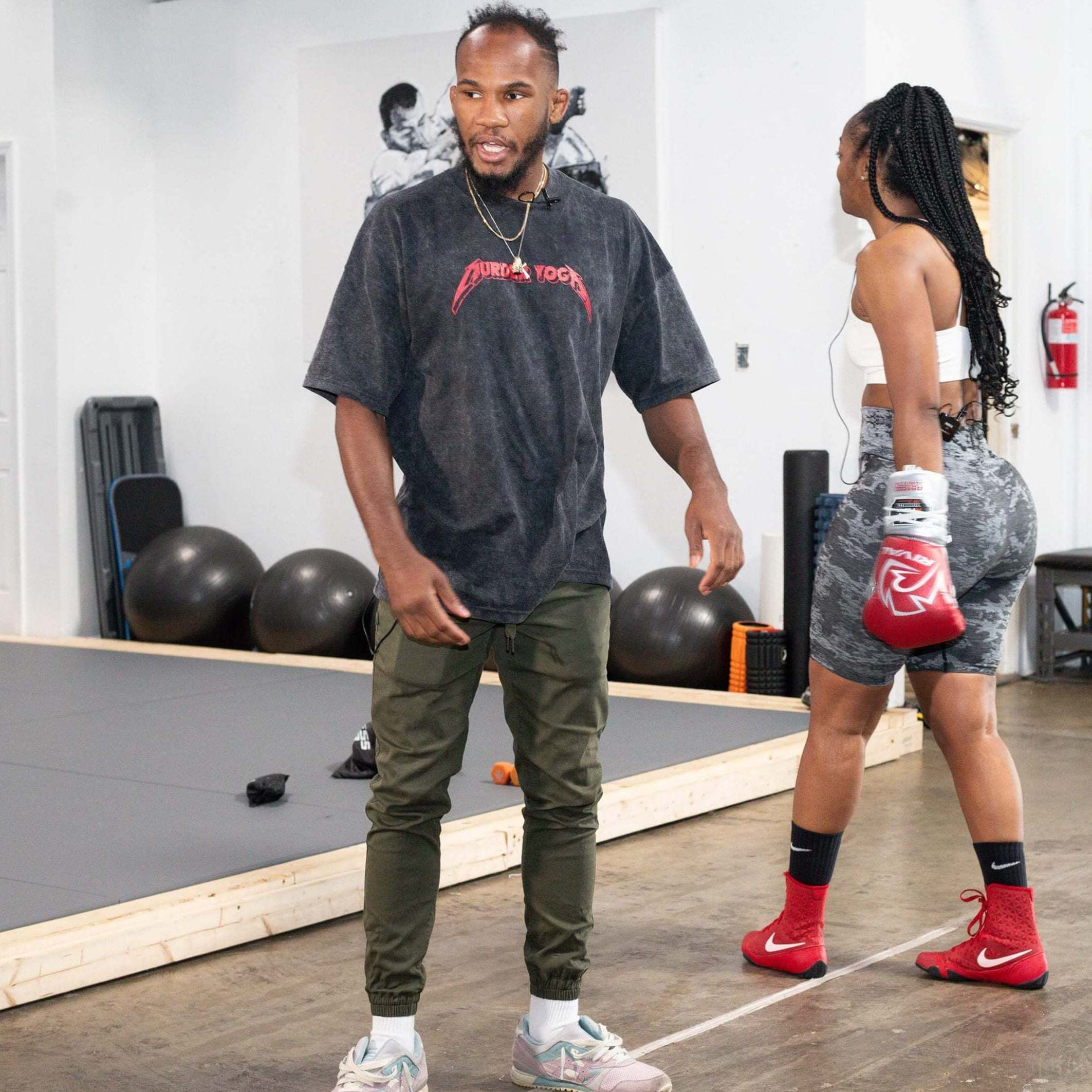 man wearing black oversized MURDER YOGA V2 BJJ t-shirt training in gym with woman boxer in red gloves