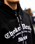 Black BJJ hoodie choke dealer with white gothic text and branding on a blurred background