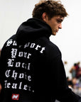 Person wearing a Black BJJ hoodie choke dealer with white gothic text and branding on a blurred background