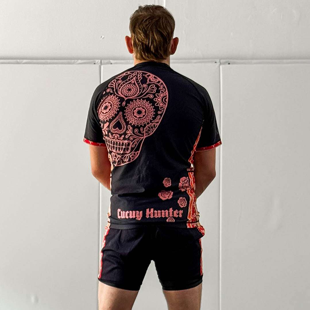 Cucuy Hunter BJJ Rash Guard Set featuring Tex-Mex-inspired design with skull artwork on back, black and red color scheme, short sleeves, and matching grappling shorts.