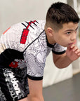 Boy wearing white and black Rising Dragon kids BJJ rash guard with short sleeves and Japanese tattoo-inspired design in training pose