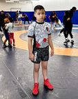 Youth wearing Rising Dragon Kids BJJ rash guard set with dragon design and black grappling shorts on wrestling mat