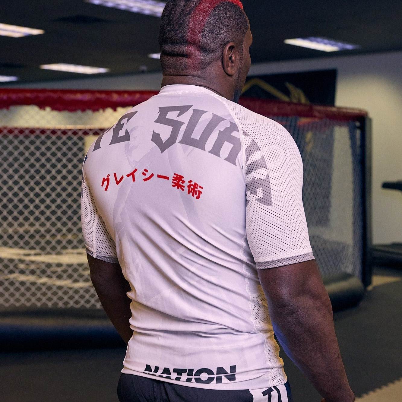 White BJJ Rash Guard with graphic design and text, worn by a person in a gym setting, showcasing durable and breathable compression fit for No-Gi Jiu Jitsu training.