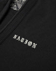 Close-up of a black textured knit Brazilian jiu jitsu kimono jacket with white embroidered 'NATION' lettering on the chest and a patterned inner neck label.