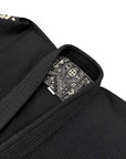 Close-up of a black martial arts bjj gi jacket with a matching black belt, showing a patterned interior label on the collar against a white background.