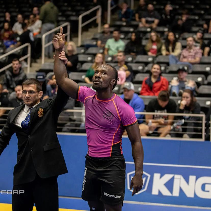 Athlete wearing purple BJJ Ranked Custom Rash Guard with black shorts in competition raising hand in victory