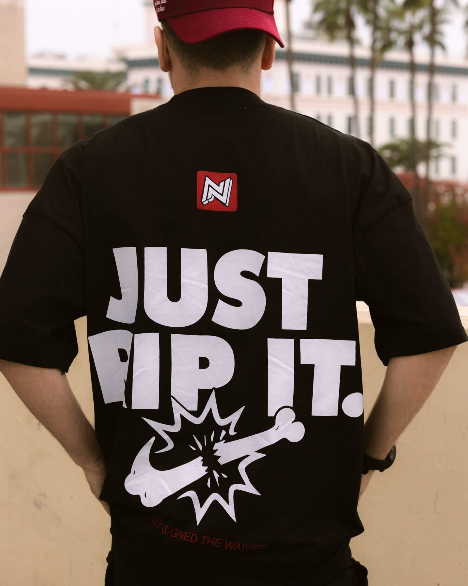 Back view of a person wearing a black, oversized BJJ shirt featuring the humorous white graphic "JUST RIP IT." with a logo breaking a bone, and "THEY SIGNED THE WAIVER." below.