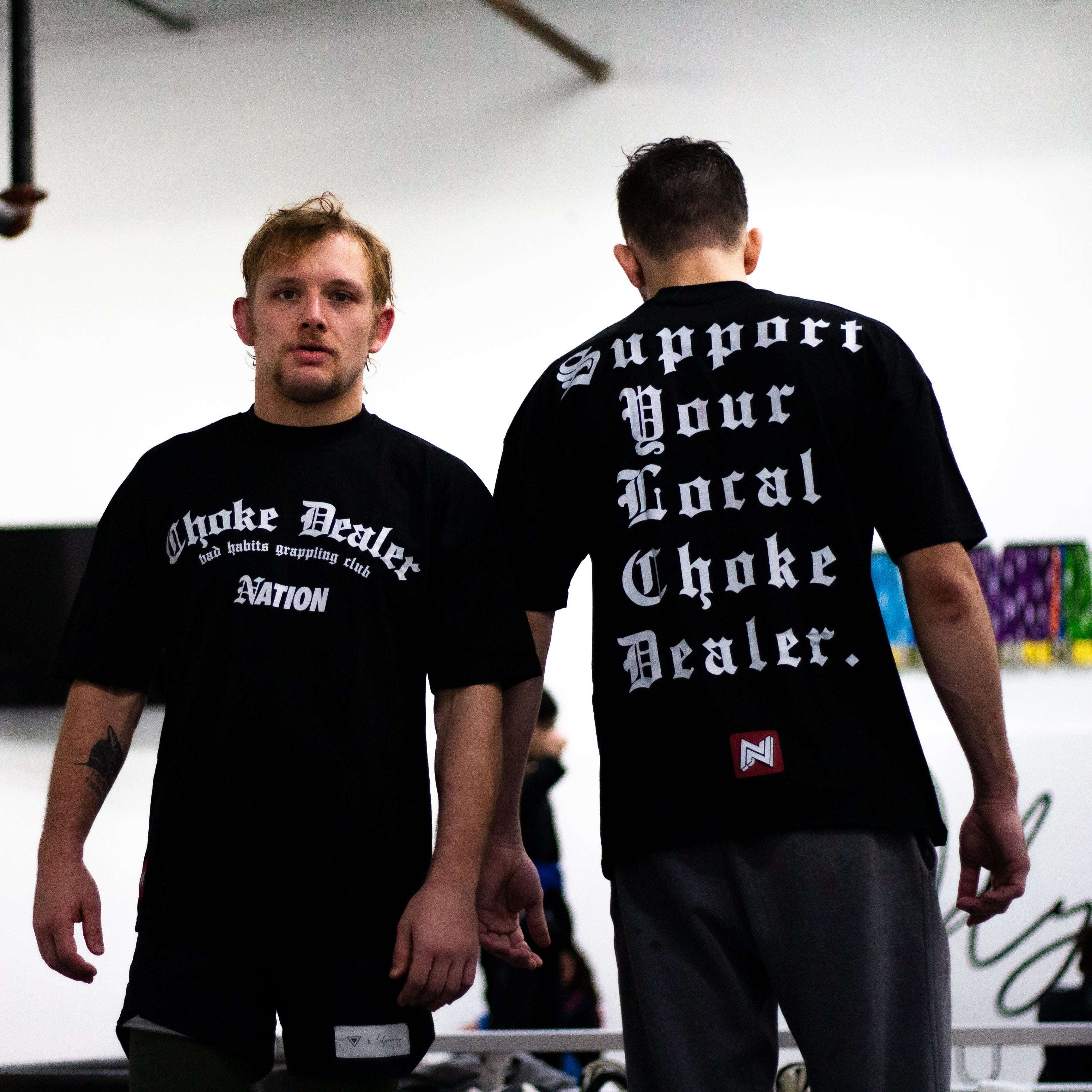 Two men wearing black t-shirts with text, standing indoors.