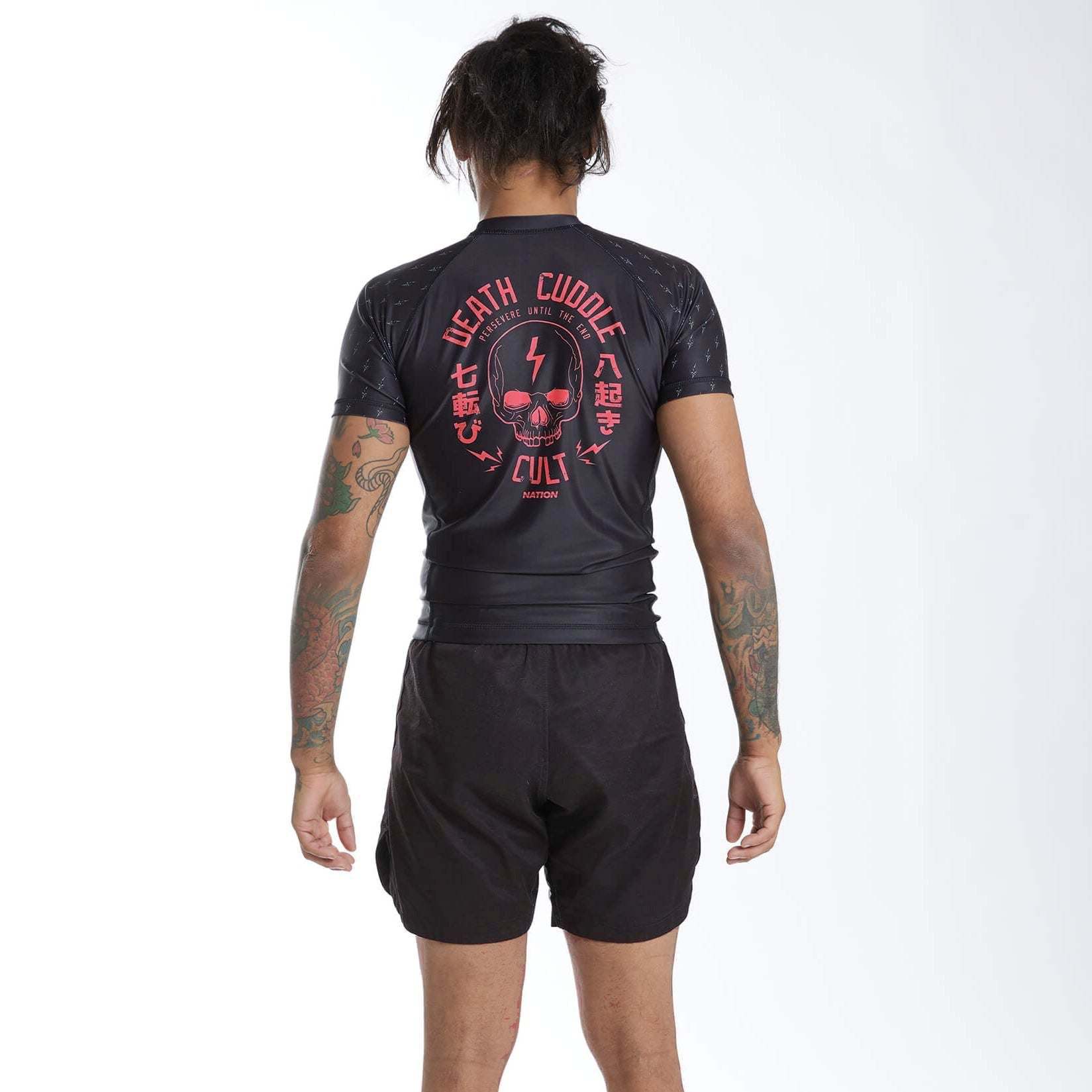 Person wearing a black Bjj rash guard set with red death cuddles Jiu Jitsu graphics on the back, standing against a white background.