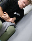 Person in a black bjj t-shirt with a logo performing a martial arts move on another person.