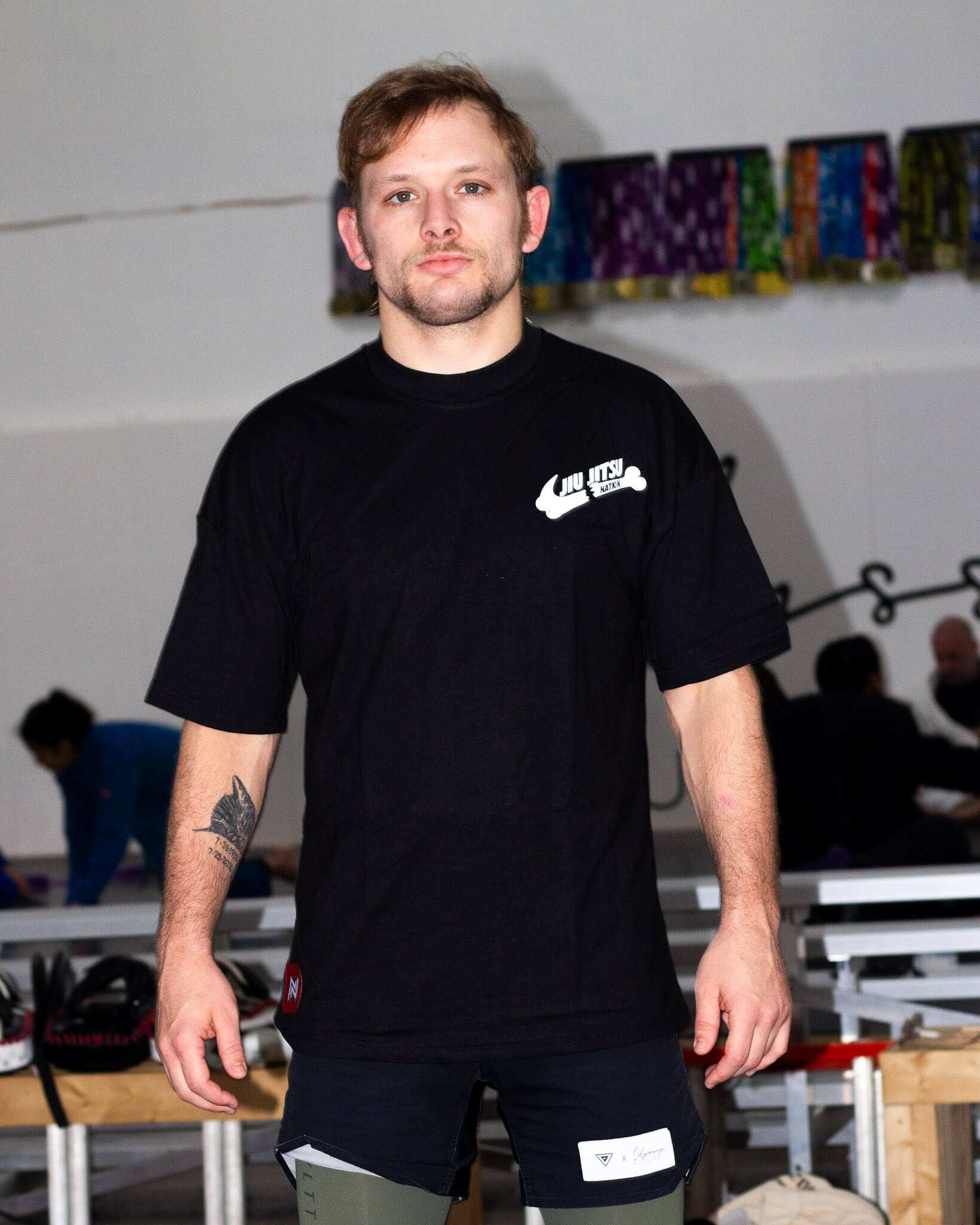 Man wearing a black bjj t-shirt with a logo in an indoor setting