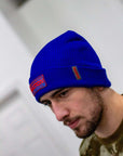 Man wearing a blue beanie with a logo on a neutral background