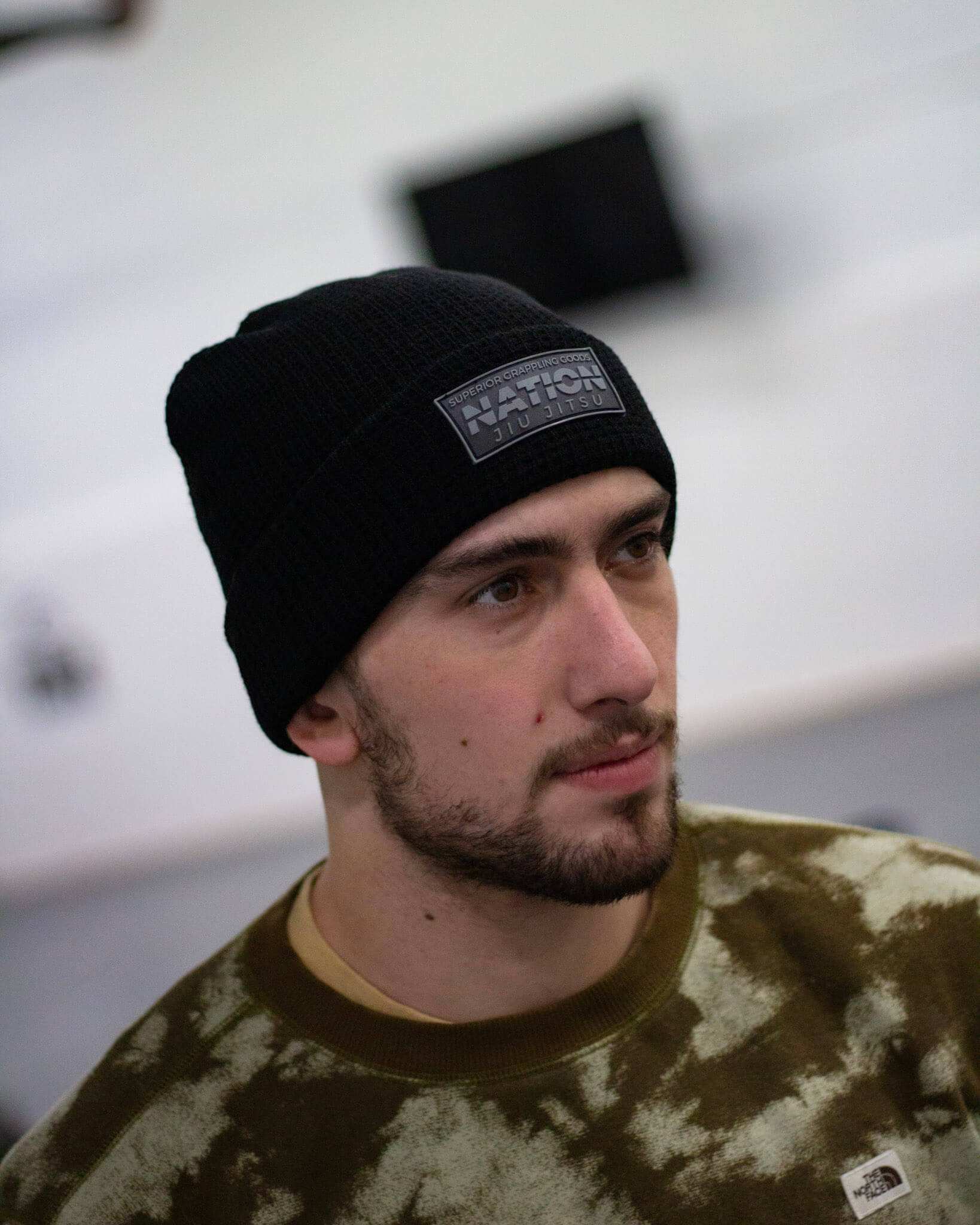 Person wearing a black beanie with a logo, looking to the side.