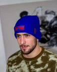 Man wearing a blue beanie with 'NATION' text, standing against a blurred background.