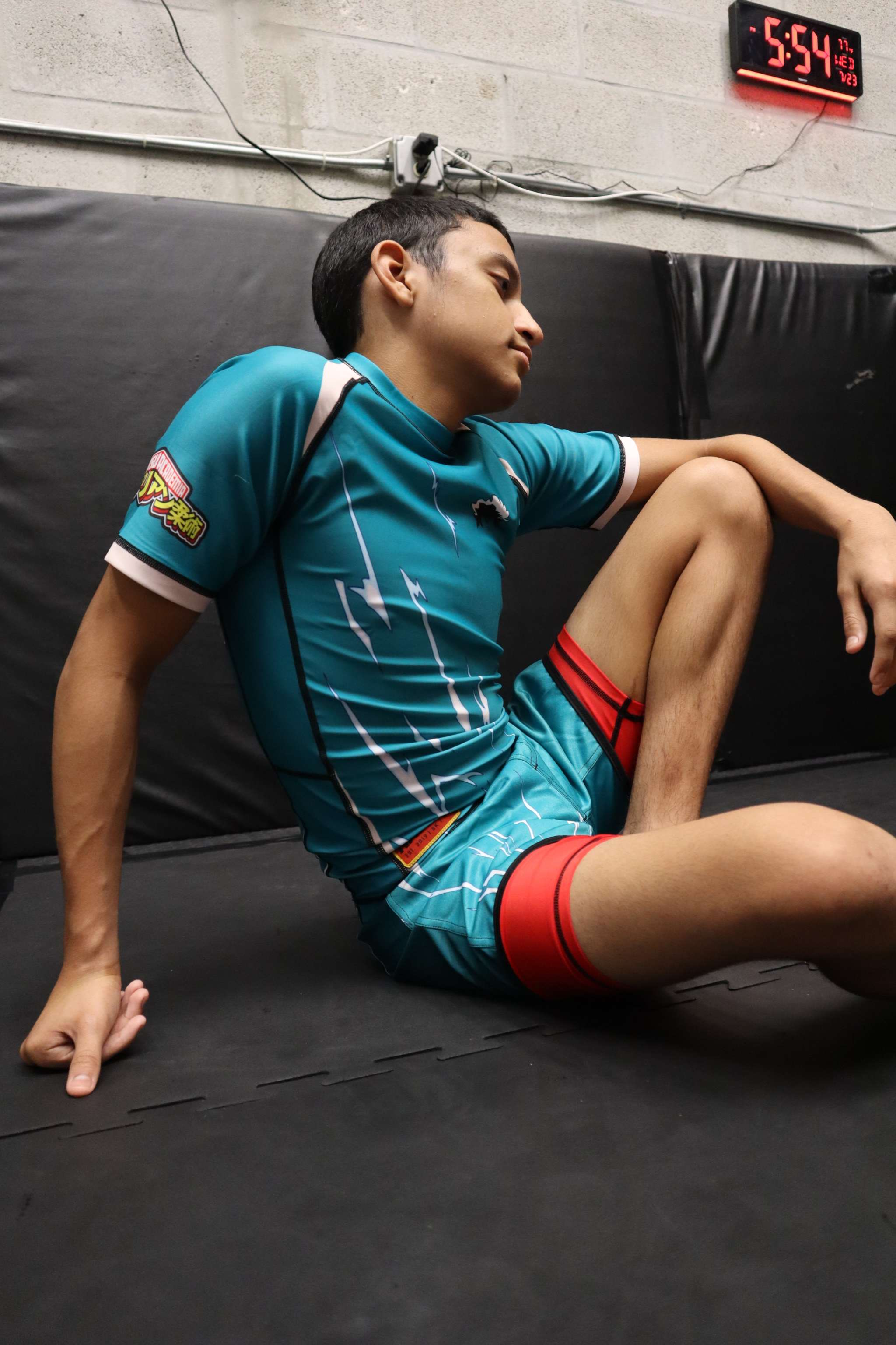 Person in a blue athletic outfit with red accents sitting on a black mat.