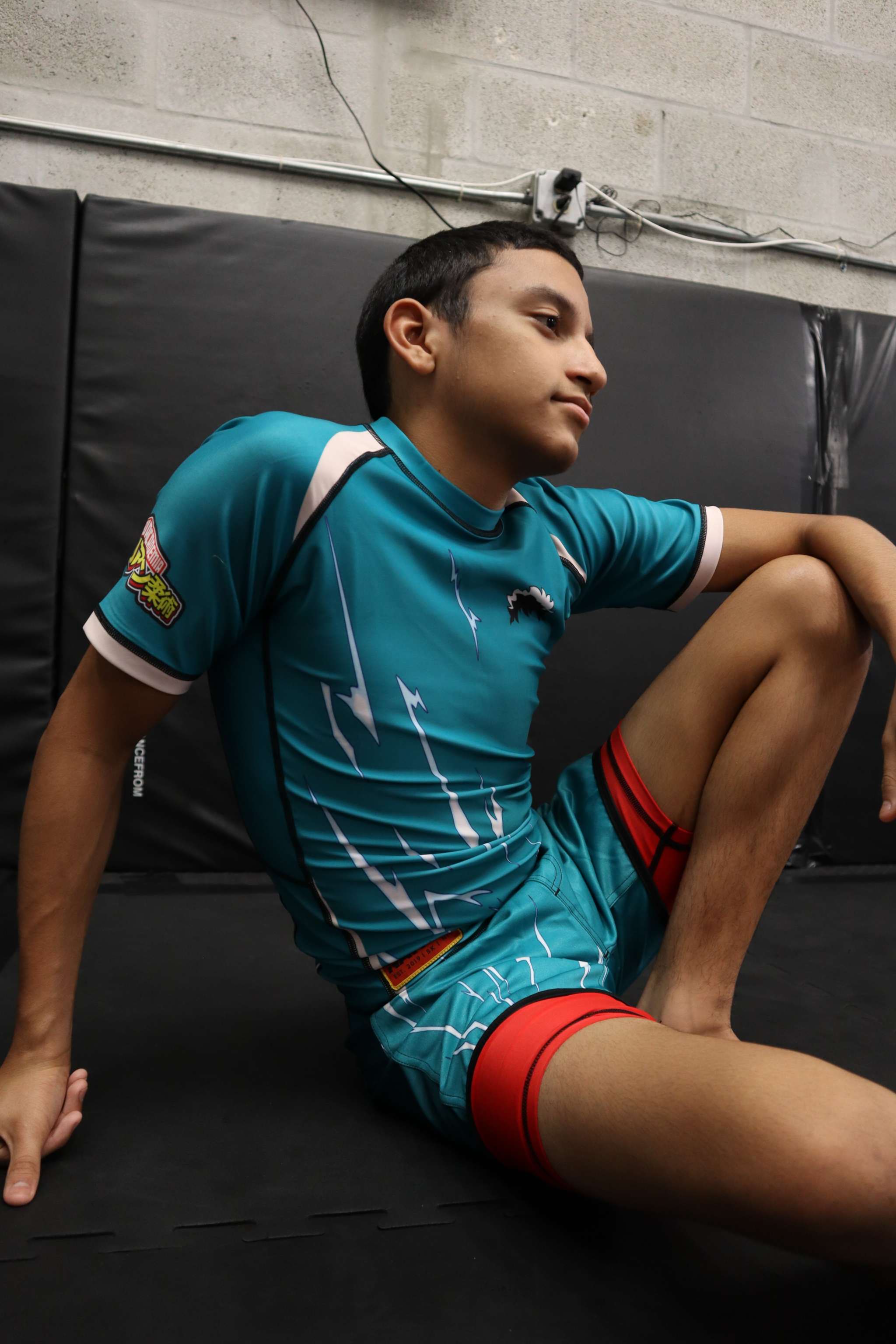 Person wearing a blue sports outfit with red accents, sitting on a black mat.