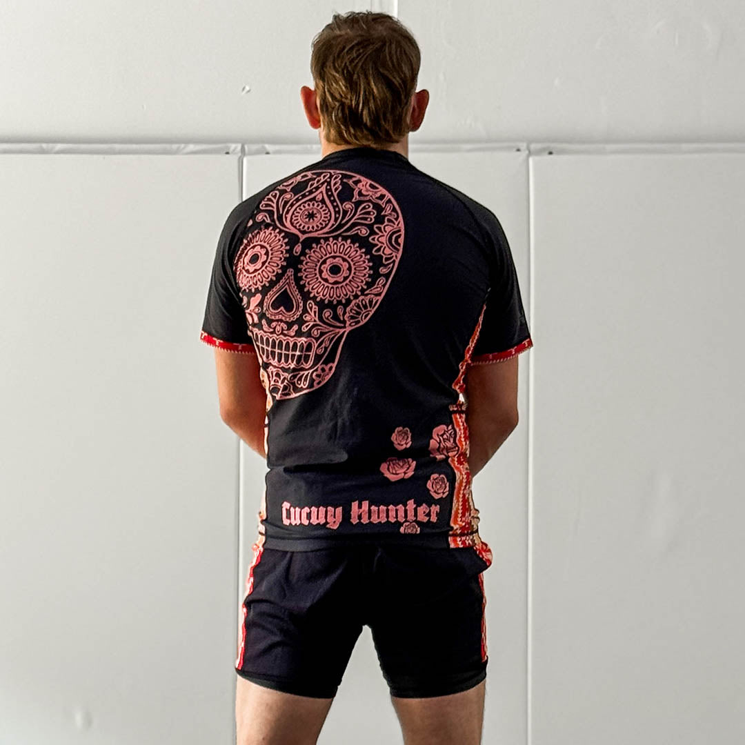 Cucuy Hunter BJJ Rash Guard Set featuring Tex-Mex-inspired design with skull artwork on back, black and red color scheme, short sleeves, and matching grappling shorts.