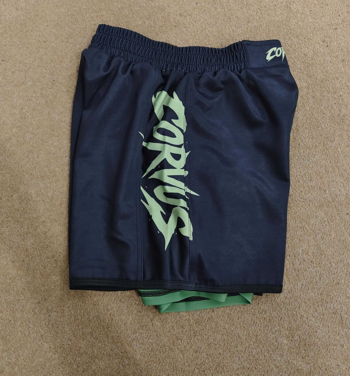 Navy shorts with green logo on a beige surface