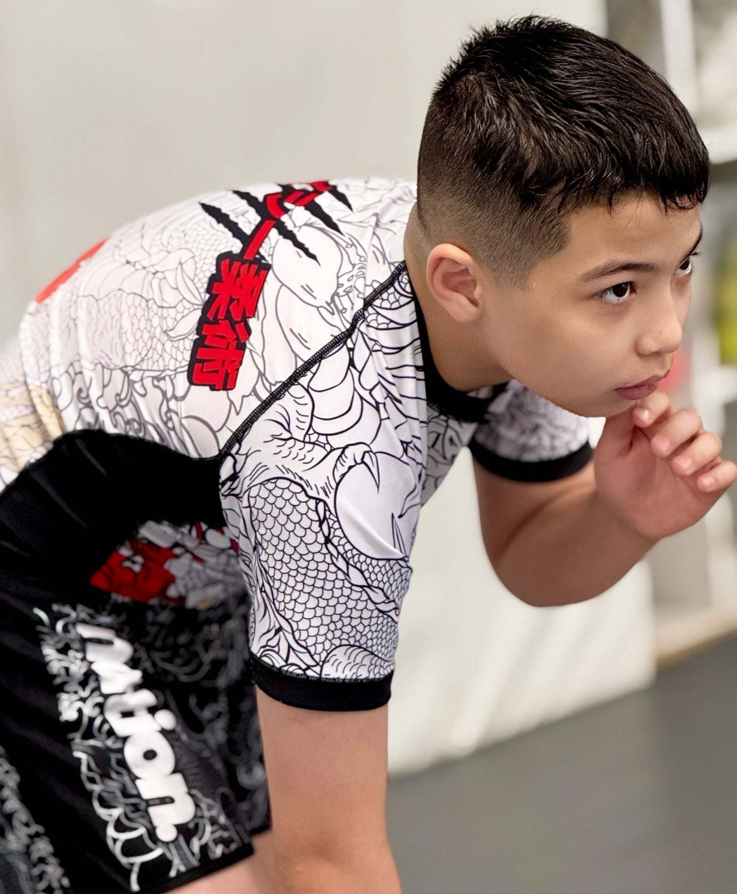 Boy wearing white and black Rising Dragon kids BJJ rash guard with short sleeves and Japanese tattoo-inspired design in training pose