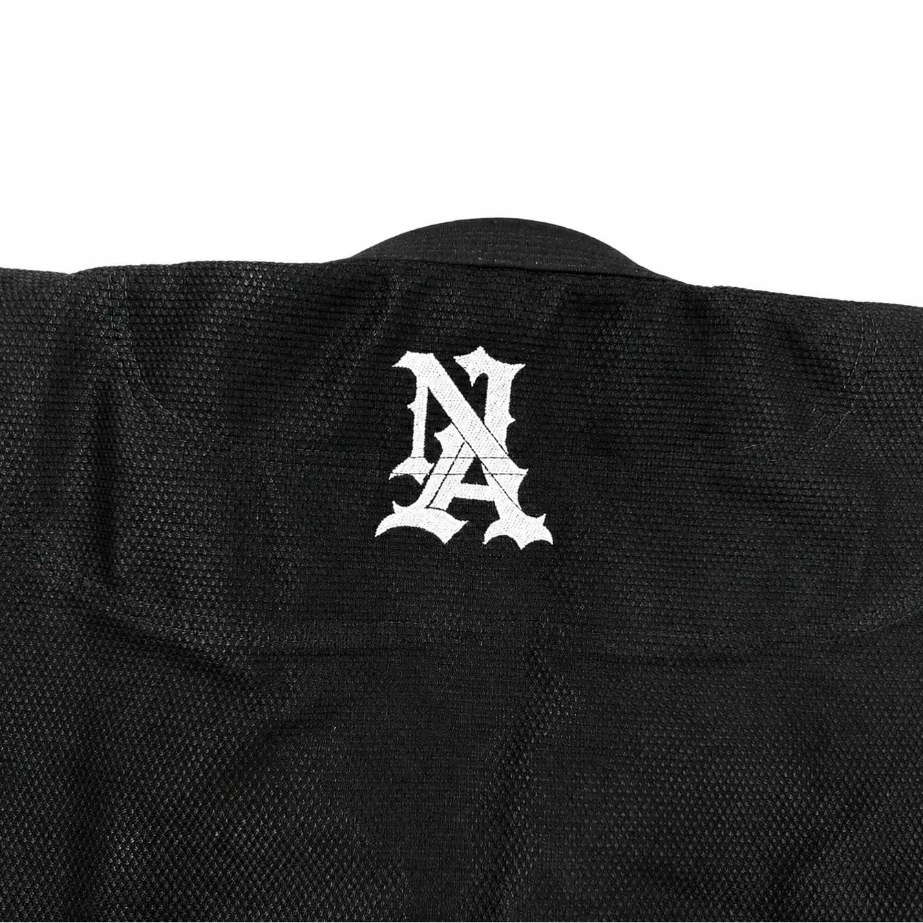 Close-up of the back of a black textured jiu jitsu kimono, featuring a white stylized 'NA' monogram logo centered on the upper back.