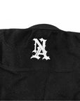 Close-up of the back of a black textured jiu jitsu kimono, featuring a white stylized 'NA' monogram logo centered on the upper back.