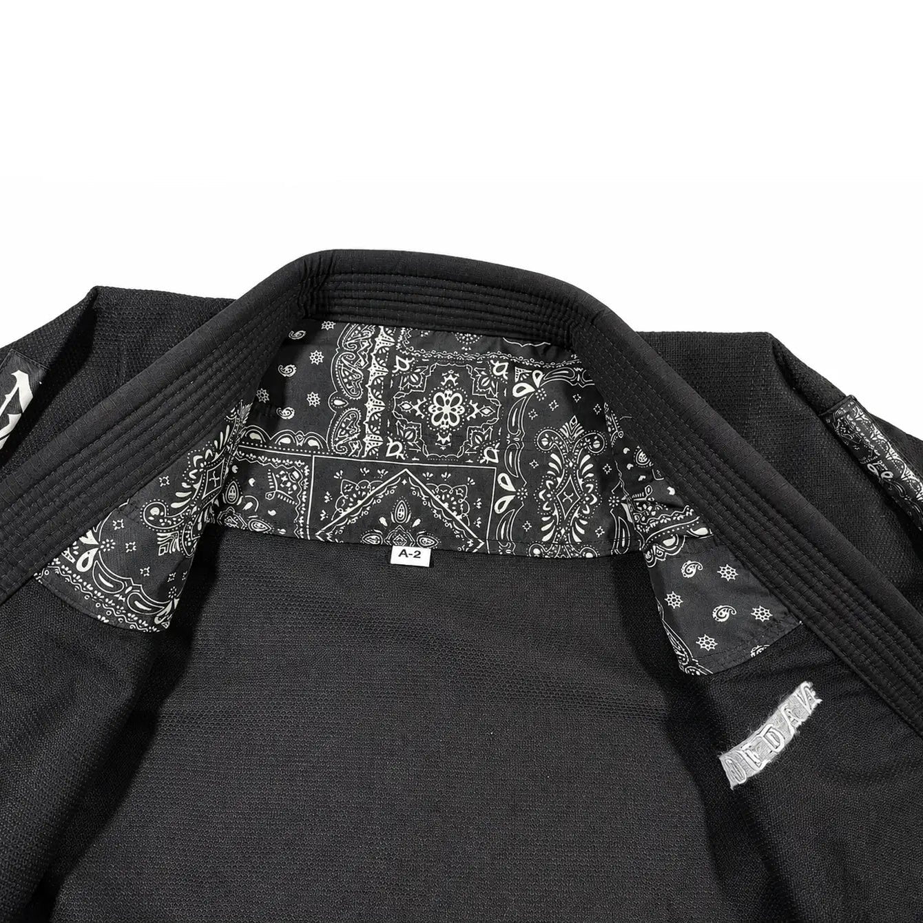 Close-up of a black martial arts jiu jitsu gi jacket with a black and white patterned bandana collar lining and a small white brand tag.