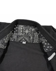 Close-up of a black martial arts jiu jitsu gi jacket with a black and white patterned bandana collar lining and a small white brand tag.