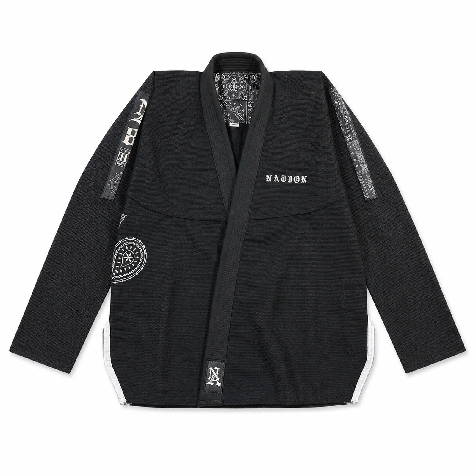 A black brazilian jiu jitsu gi jacket with white accents, featuring the brand name 'nation' on the chest, white text down one sleeve, and circular patches on the front and sleeve, laid flat against a white background.