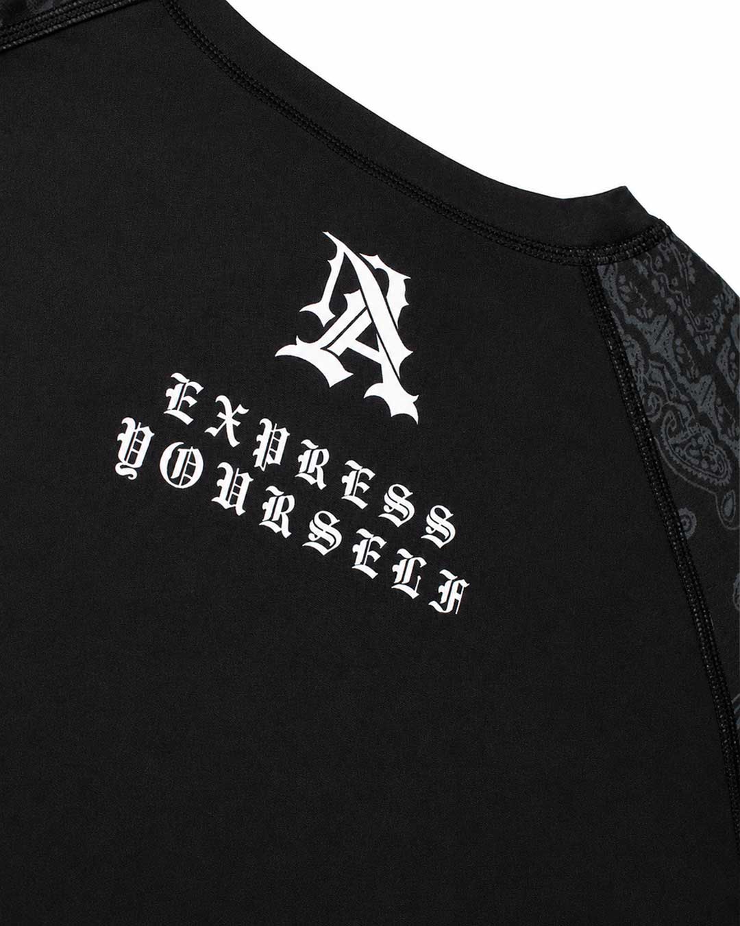 Close-up of a black BJJ Rash Guard shirt featuring a white Gothic-style monogram 'A' and the text 'Express Yourself' printed on the chest, with black lace-like patterned sleeves.