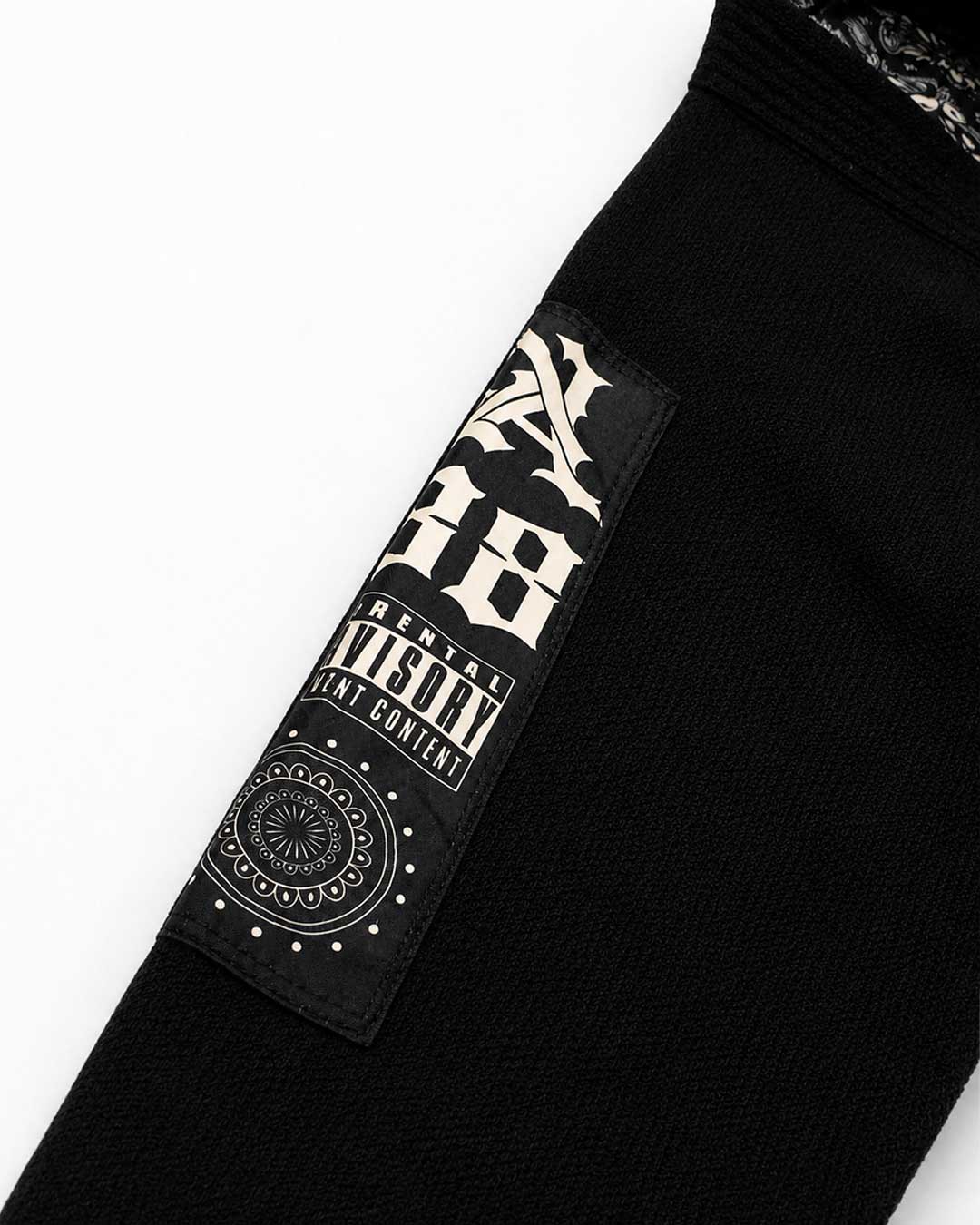 Close-up of a black Brazilian jiu jitsu kimono jacket sleeve featuring a rectangular black patch with a cream graphic design and the words 'Parental Advisory' and 'Rental Content'.