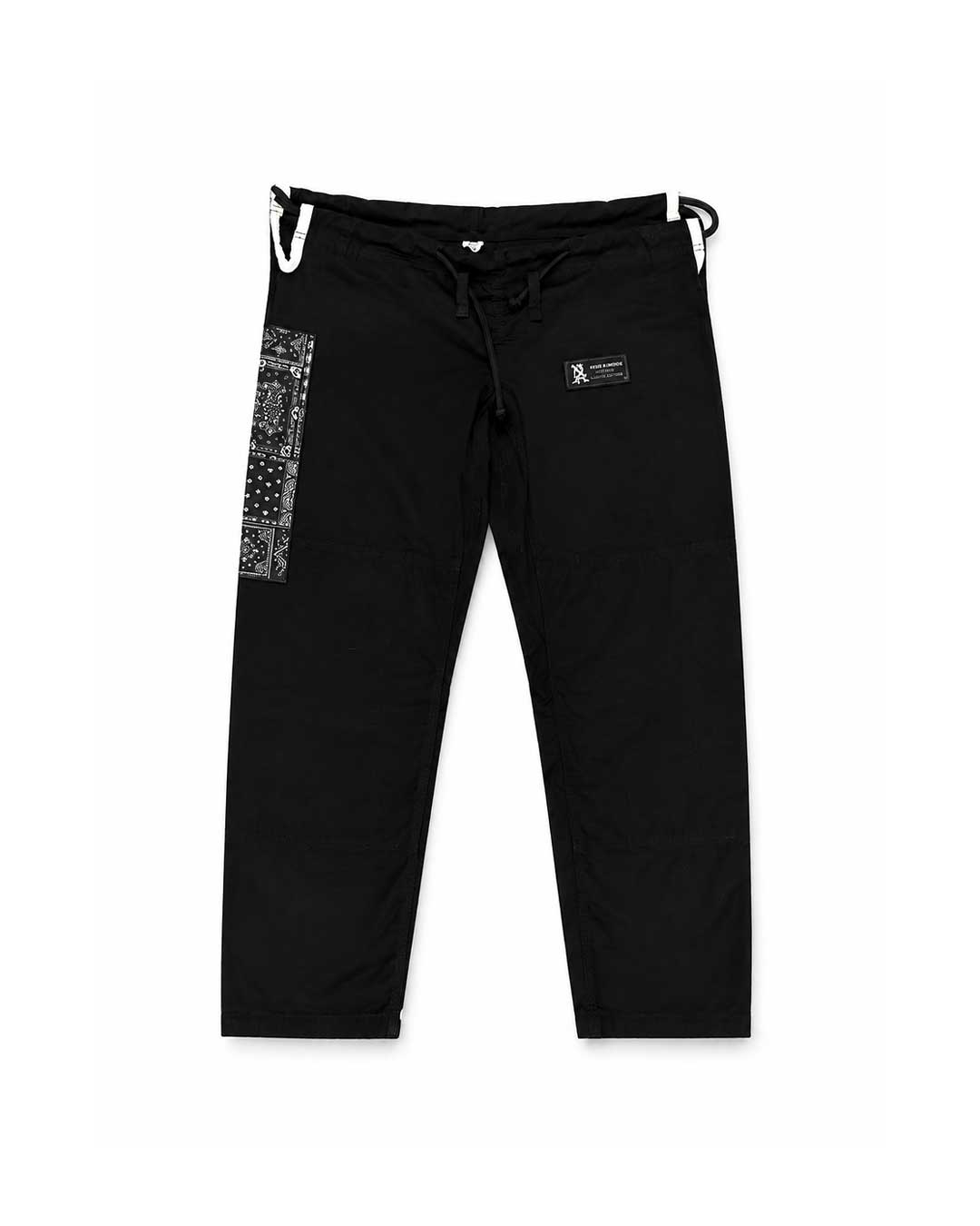 Black Brazilian jiu jitsu kimono pants with a drawstring waist, featuring a vertical black-and-white patterned panel on the left leg and a small black brand patch on the right thigh, shown against a plain white background.