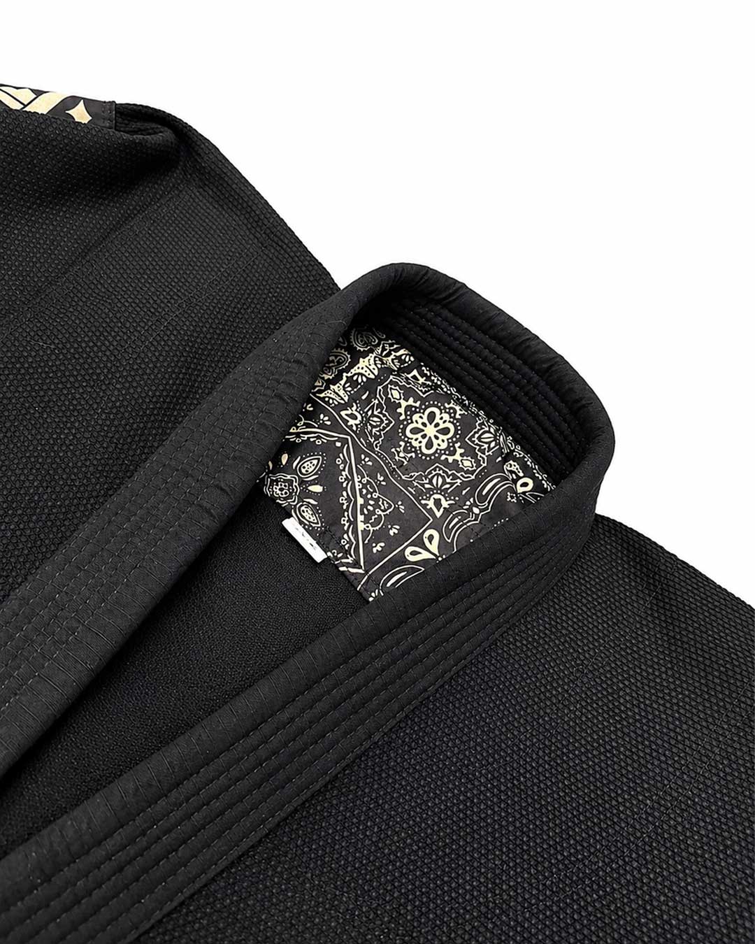 Close-up of a black martial arts bjj gi jacket with a matching black belt, showing a patterned interior label on the collar against a white background.