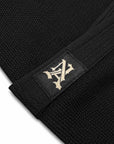 Close-up of a black Brazilian jiu jitsu gi item with a black strap featuring a beige embroidered stylized logo patch.