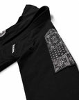 Close-up of a black jiu jitsu gi jacket laid flat on a white background, featuring a large black-and-white bandana print patch on the sleeve and small white logo text on the side.