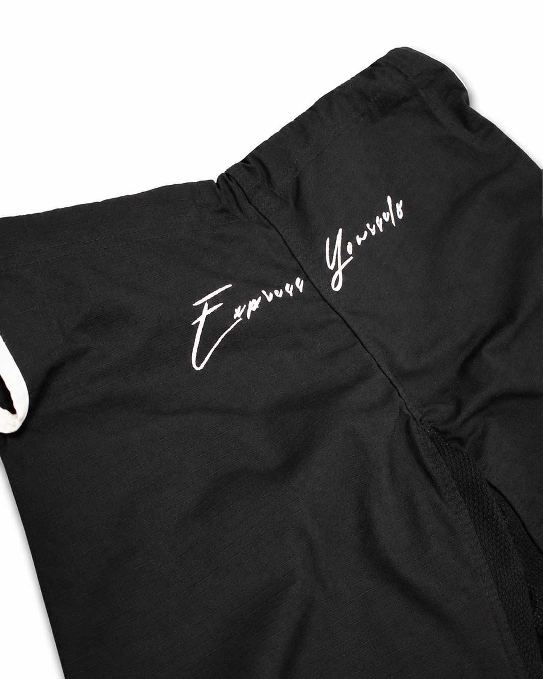 Close-up of black bjj gi pants with white script embroidery reading 'Express Yourself' on the thigh, shown against a plain white background.