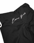 Close-up of black bjj gi pants with white script embroidery reading 'Express Yourself' on the thigh, shown against a plain white background.