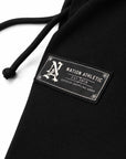 Close-up of a black ribbed fabric garment with a black drawstring and a rectangular sewn patch reading NATION ATHLET EST. 2019 SUPERIOR GRAMPLING GOODS on a white background.